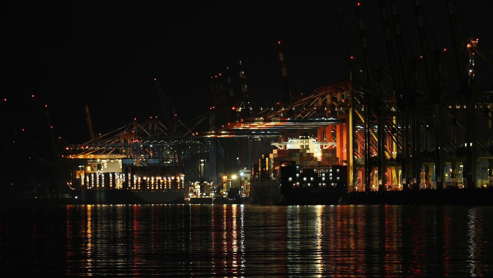 Port cranes illuminated at night reflected in the water